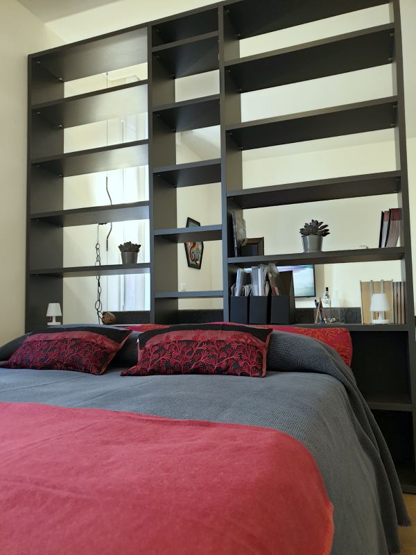 Double bed with a red bedspread behind the open bookcase